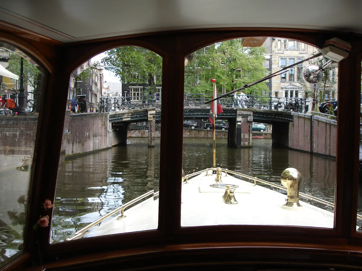 Uitzicht door de ramen van een rondvaartboot op een brug over een Amsterdamse gracht.