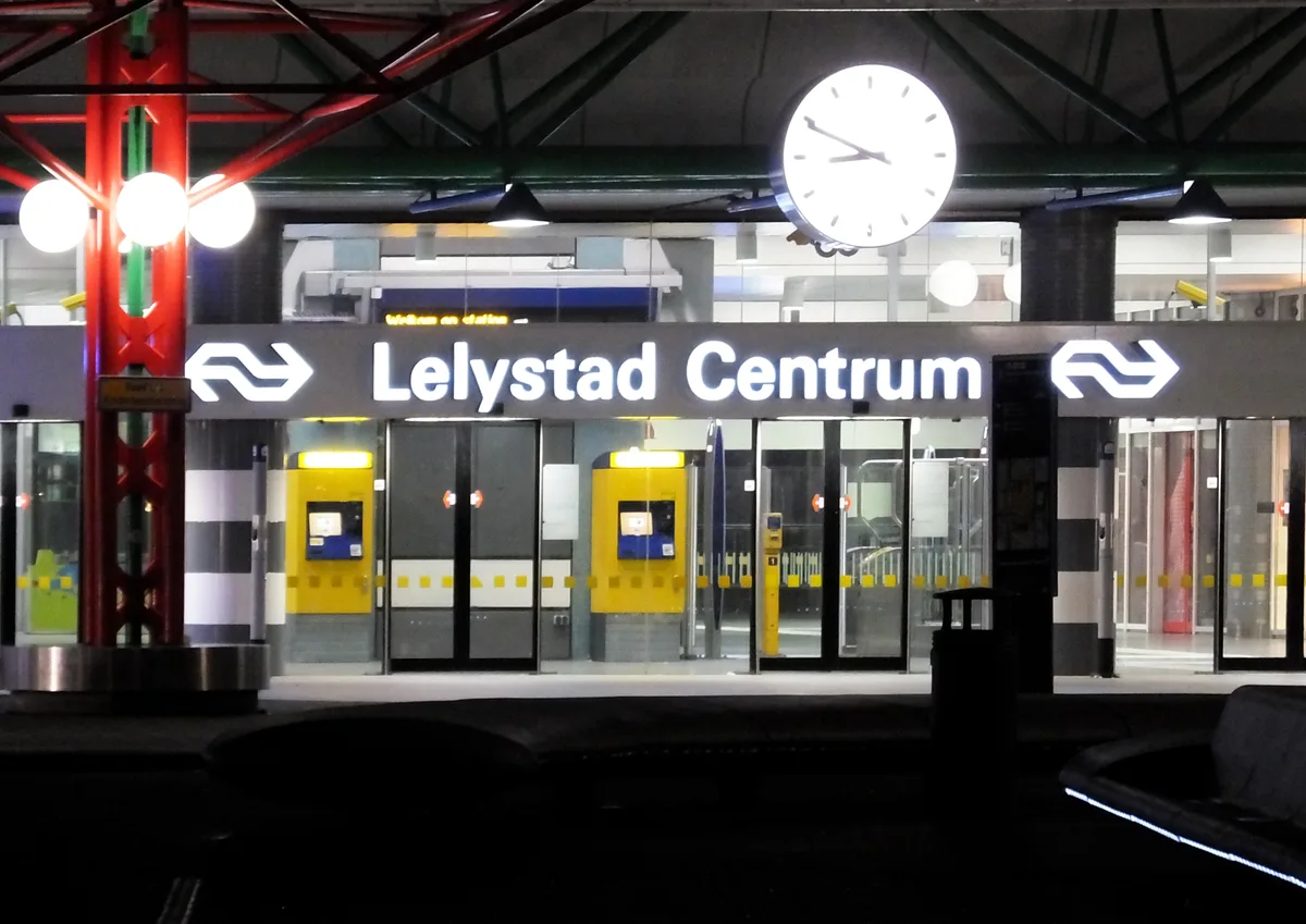 Verlichte ingang van station Lelystad Centrum met stationsnaam en klok in de avond.