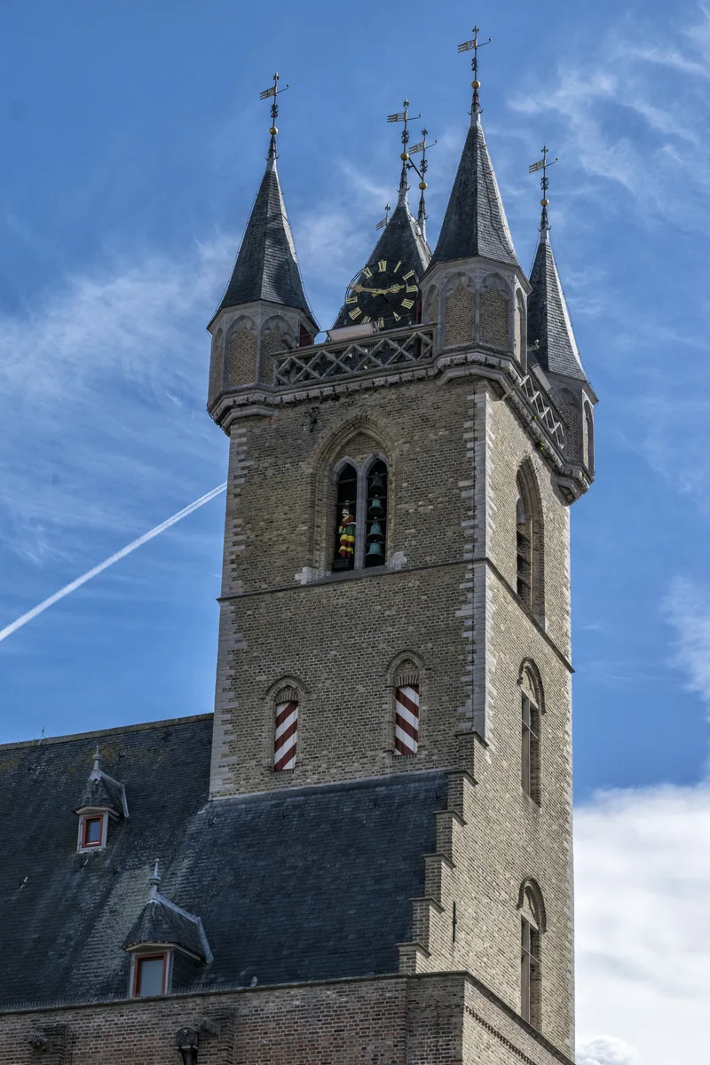 Opwaarts zicht op de toren van het Belfort tussen gebouwen in Sluis.