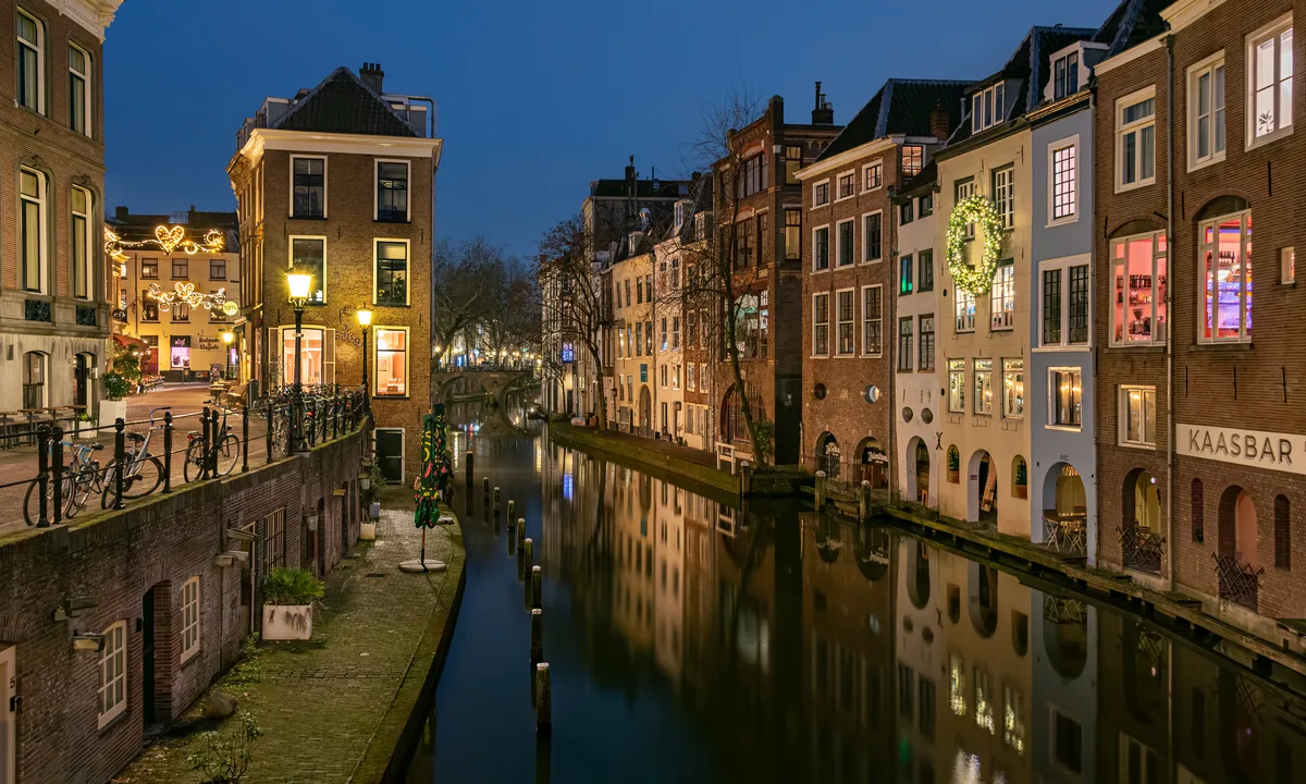 Oudegracht in Utrecht in de avondschemering met verlichte werfkelders en winterse versiering.